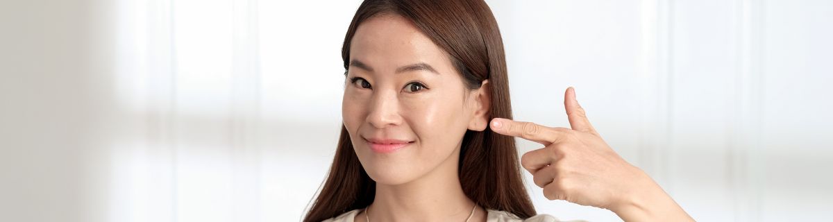 Woman pointing to one ear, representing hearing aids for one-sided hearing loss